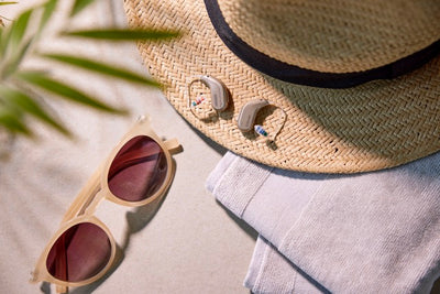Zwei Oticon Intent Hinter-dem-Ohr-Hörgeräte neben Sommeraccessoires