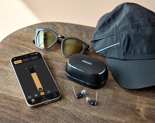 Oticon Zeal Im-Ohr-Hörgeräte auf einem Tisch neben einem Smartphone