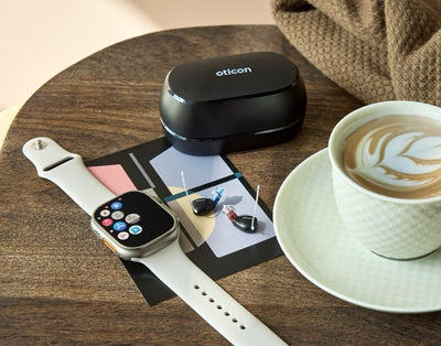 Oticon Zeal Im-Ohr-Hörgeräte auf einem Tisch neben einer Smartwatch