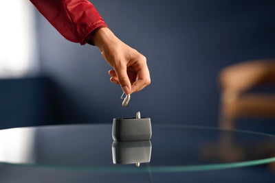Eine Hand hält ein ReSound Savi Hinter-dem-Ohr-Hörgerät über einer Ladestation