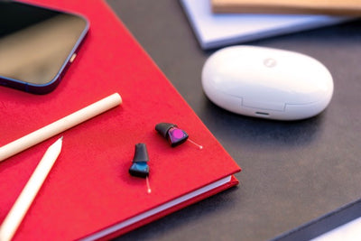 Zwei Signia Silk Charge&Go IX Im-Ohr-Hörgeräte liegen auf einem Schreibtisch